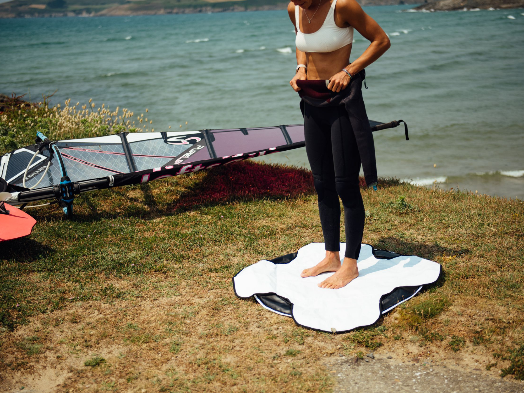 Windsurfer taking her wetsuit off outside on a changing mat with sail in background