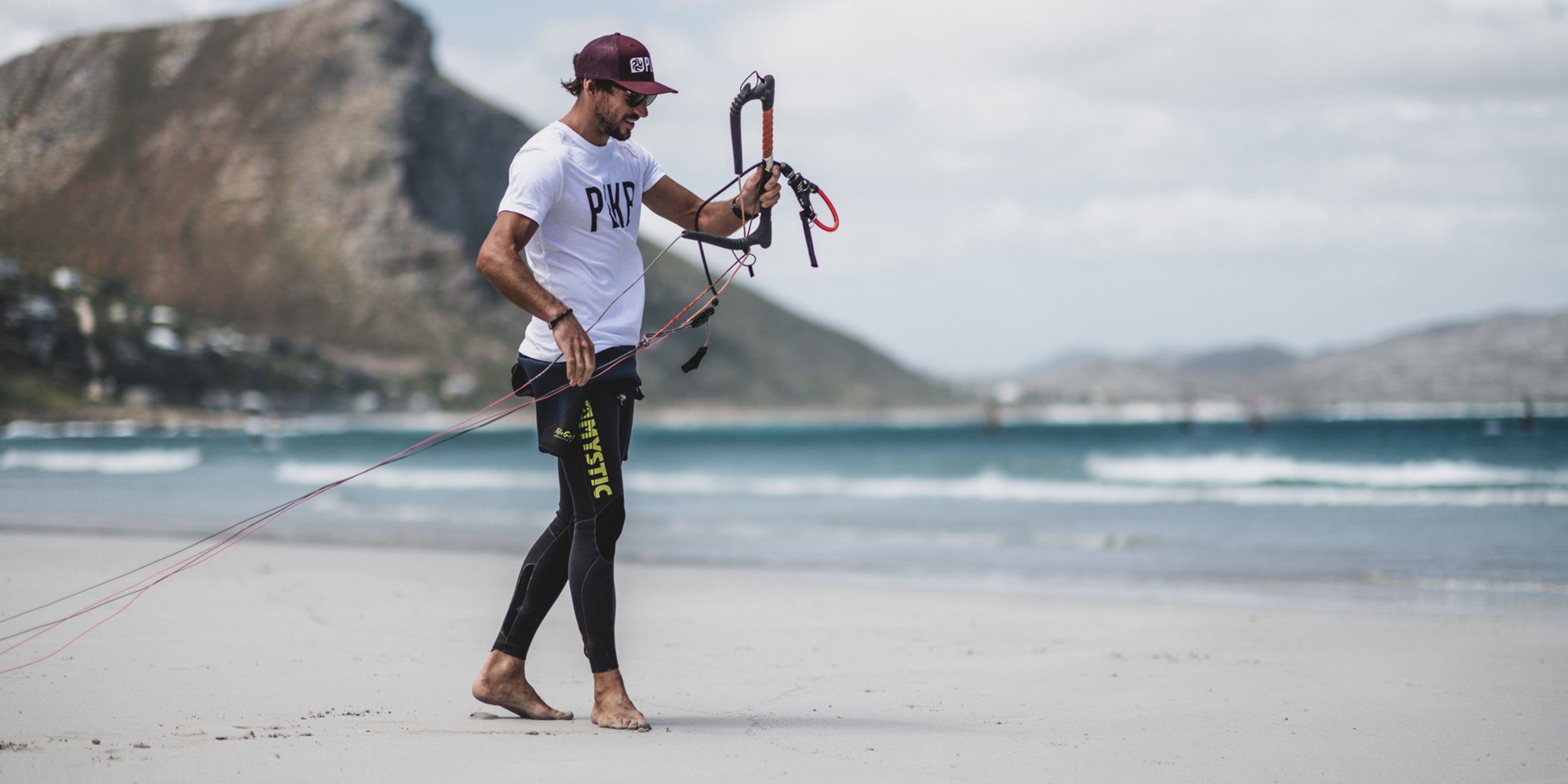 a kitesurfer holding his bar and line on a beach