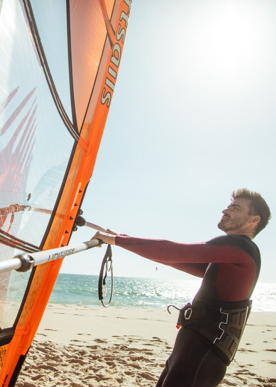 Side view of a windsurfer on beach holding an orange sail from Loftsails in Tarifa