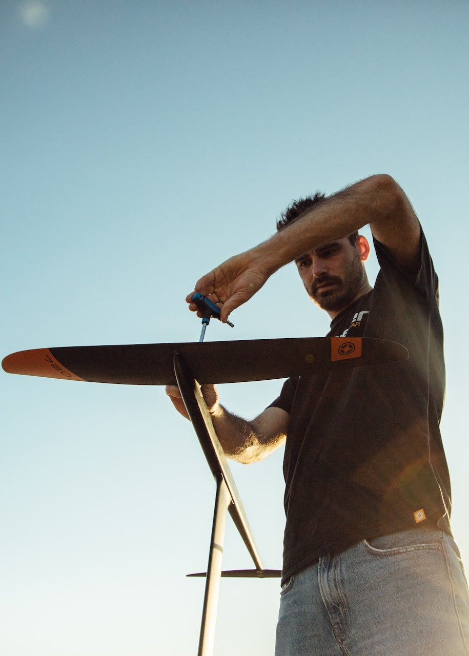 Silhouette of a person adjusting winfsurf foil equipment against a bright sky