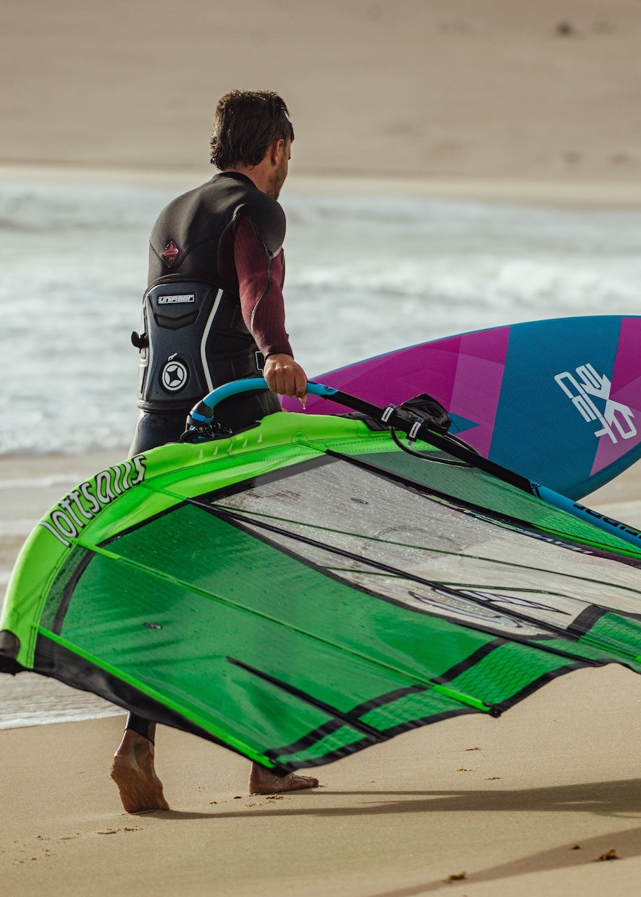 Windsurfer carrying a green sail on sandy beach