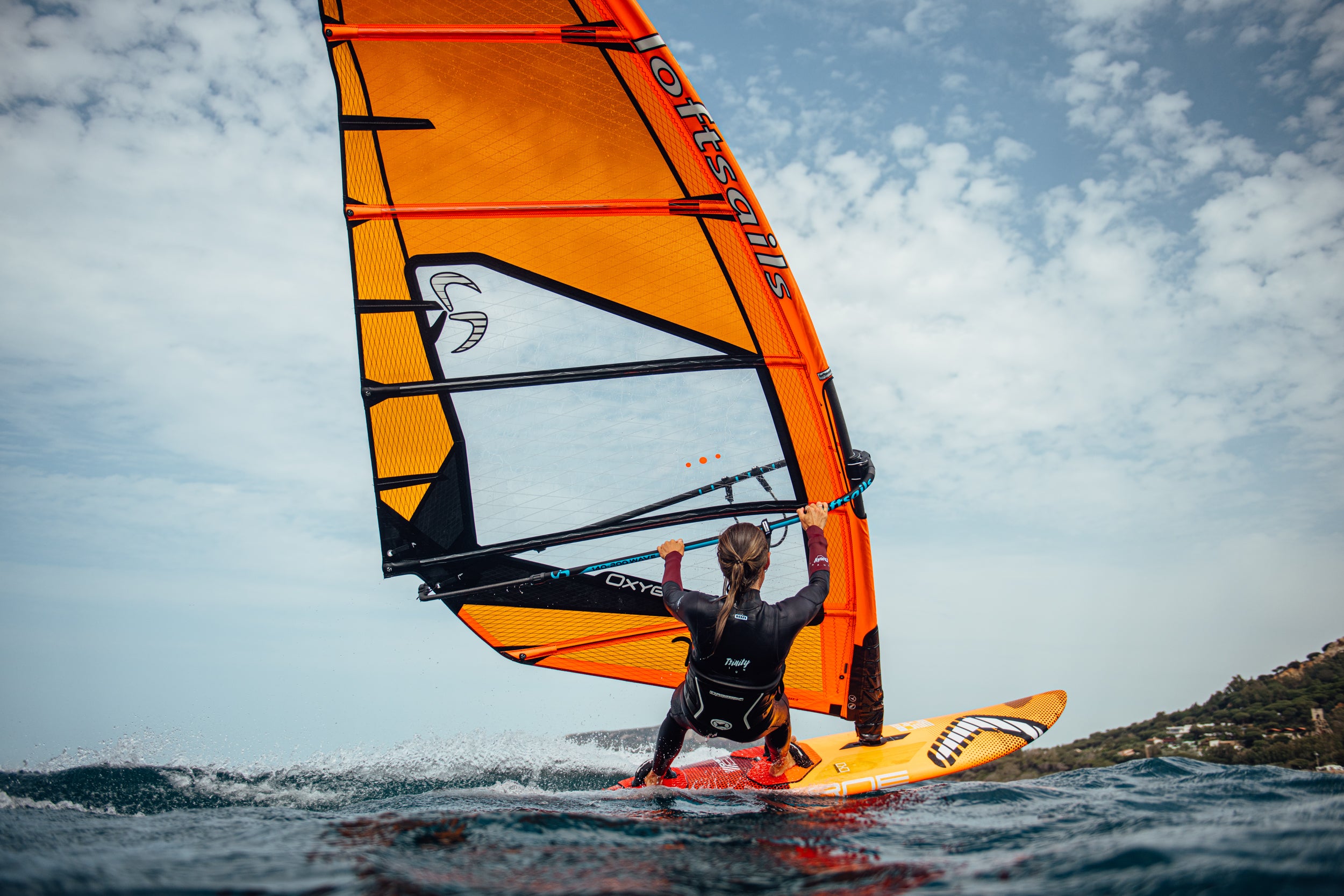 A girl windsurfing in planing mode with harnes and footstrap in action with orange sail from loftsails Oxygen and on severne windsurf board