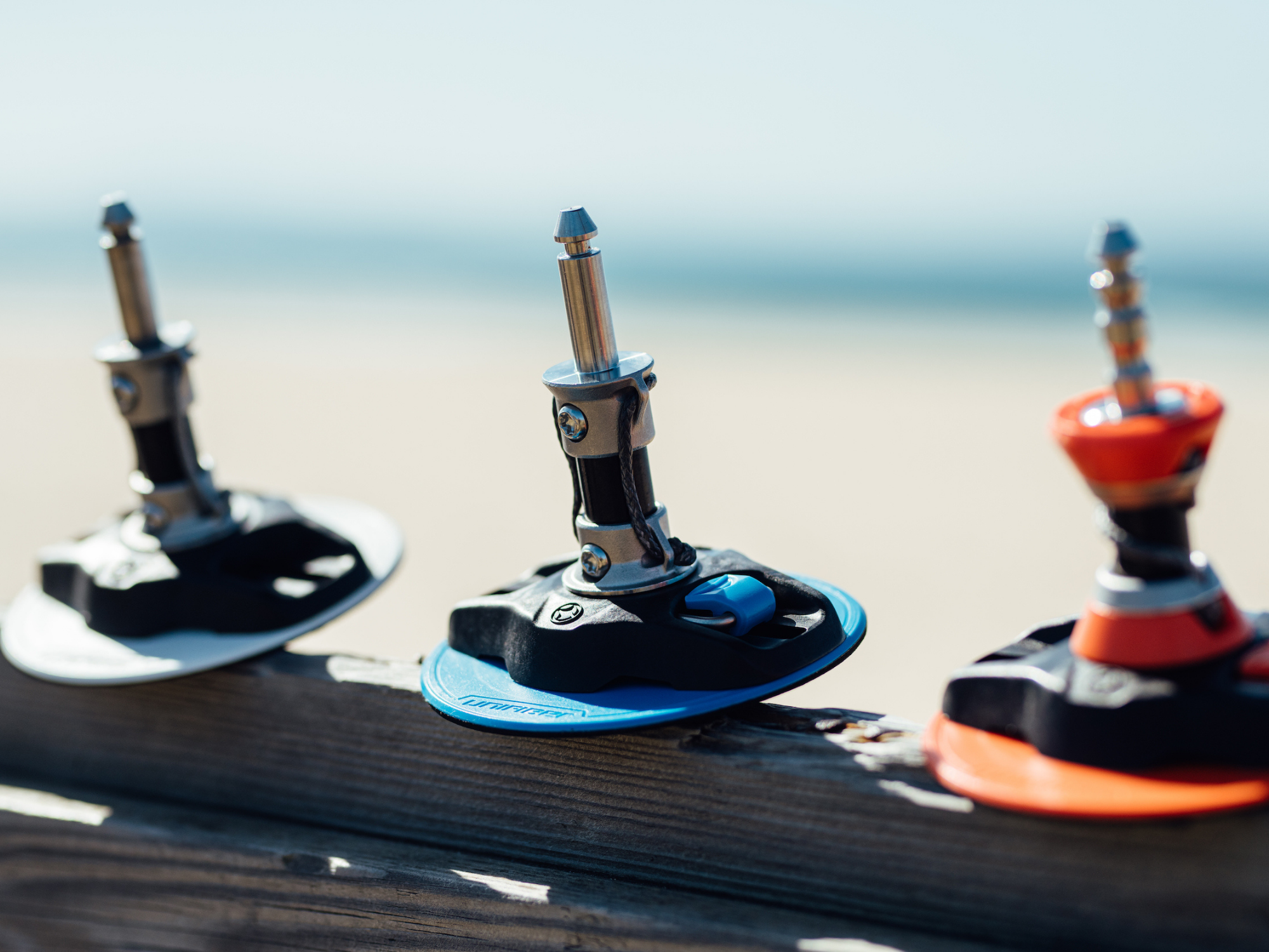 Unifiber windsurf baseplates compared: High-performance red, blue and black baseplates displayed on beach