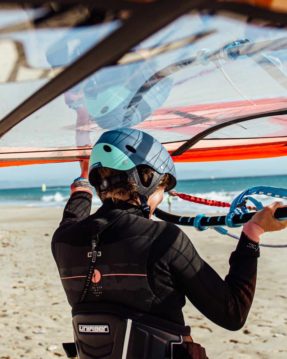 windsurfer carrying a red freeride sail on the head with a helmet and on Ion impact vest on the beach in Tarifa