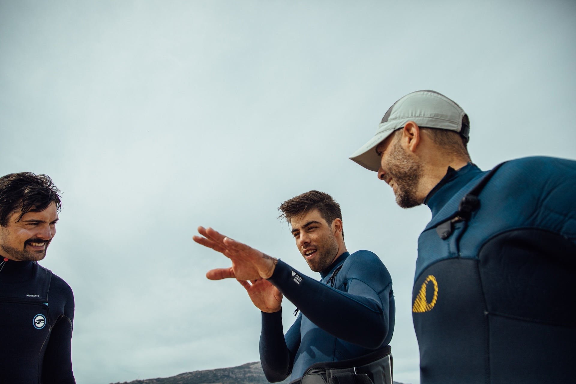 Close-up of two people in wetsuits having an animated conversation, one gesturing expressively while explaining somethin