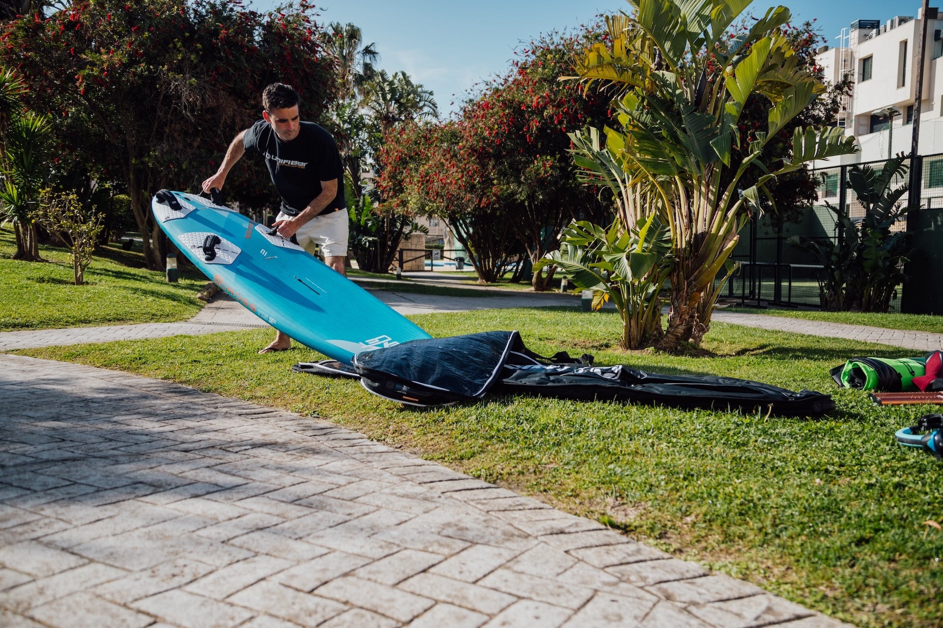 a winfsurfer putting an exocet freeride board into a travel bag on the grass