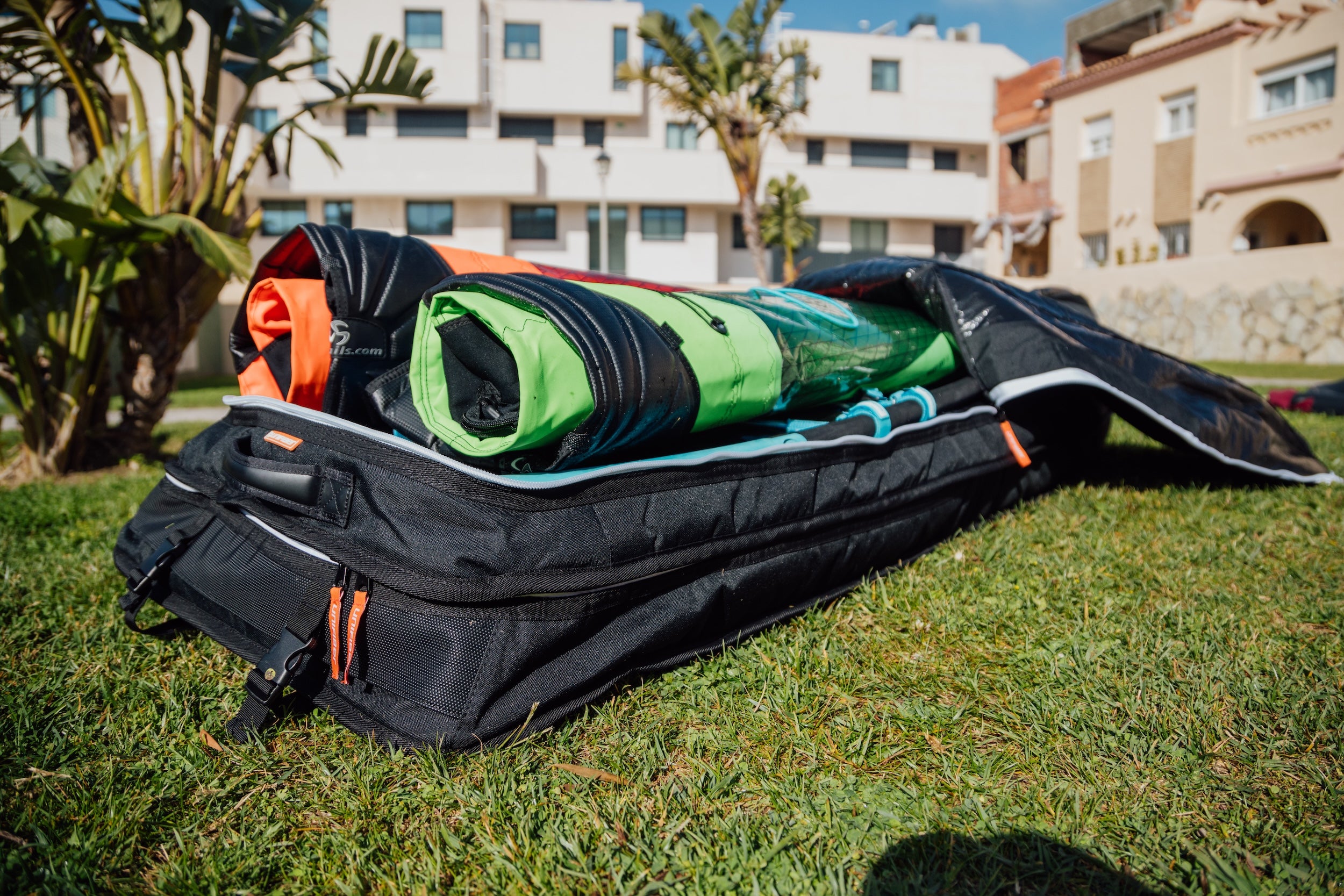 Close-up detail shot of a black and gray Pro windsurf gear bag with reinforced padding, lying open on grass with windsurf sails inside