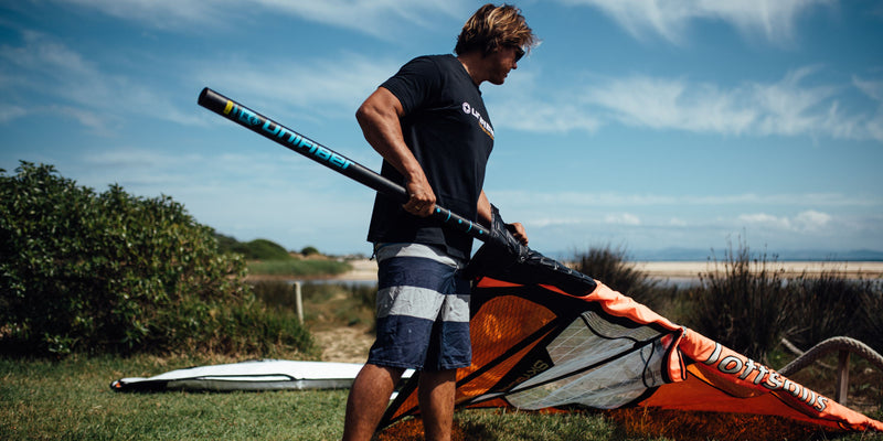 a windsurfer putting a windsurf mast into the sail when rigging on the grass 
