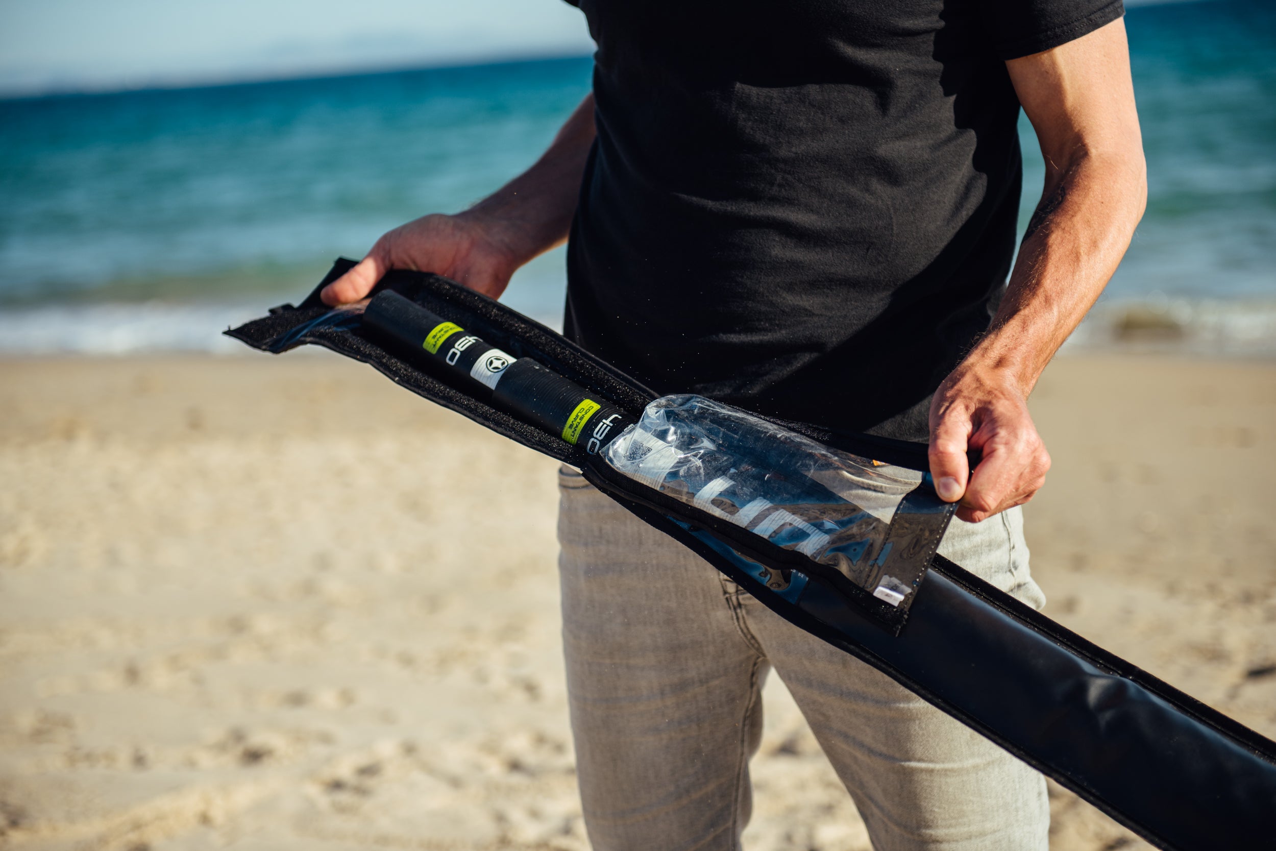 A windsurfer on the beach holding a mast bag cover with a carbon inside