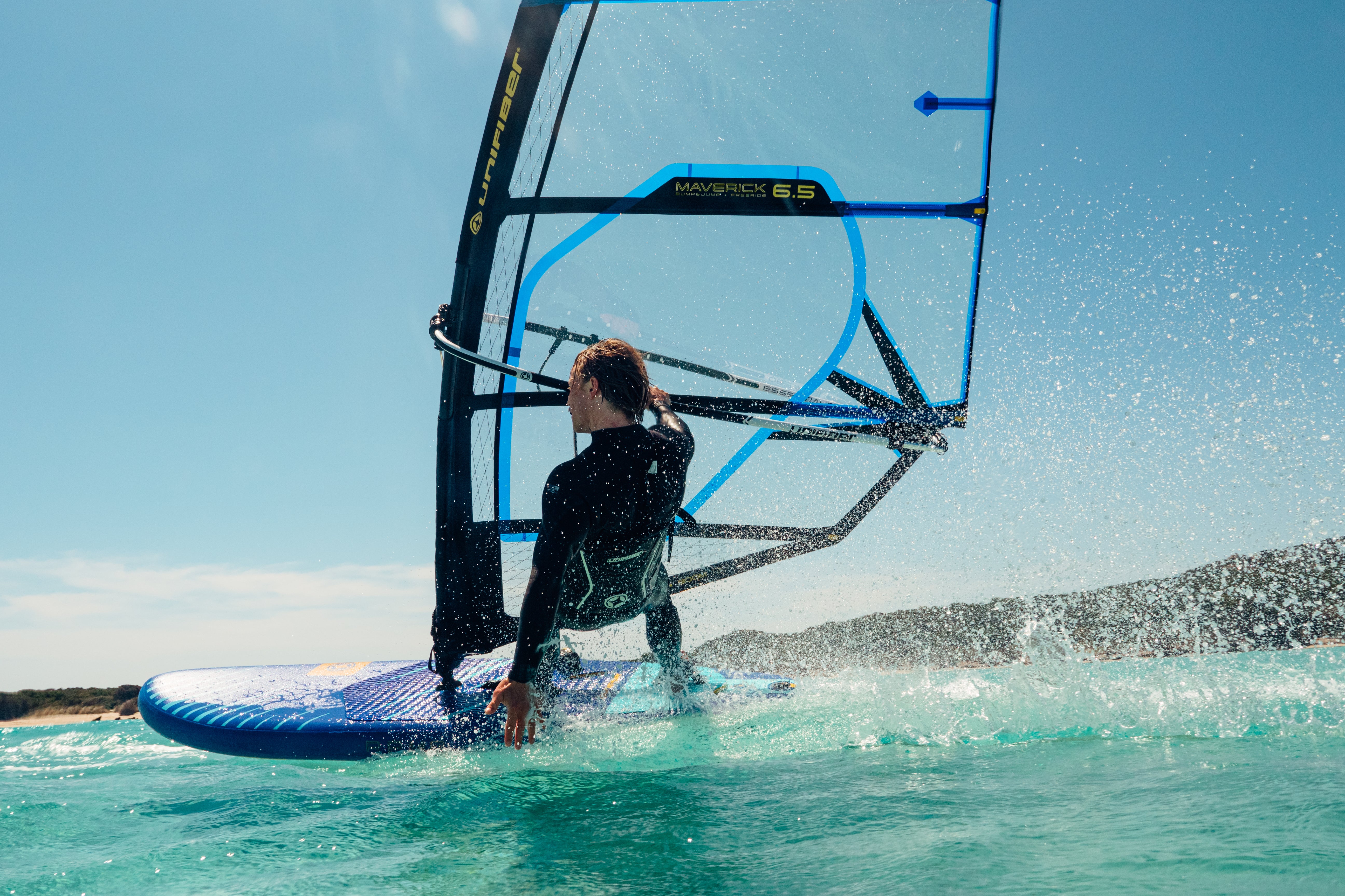 a windsurfer using an inflatable windsurf board in planing mode on clear water The sail is blue with clear monofilm structure